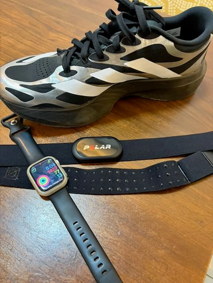 Polar heart-rate chest strap, Apple Watch, and running shoe arranged on a wooden table for a post about heart-rate training data.
